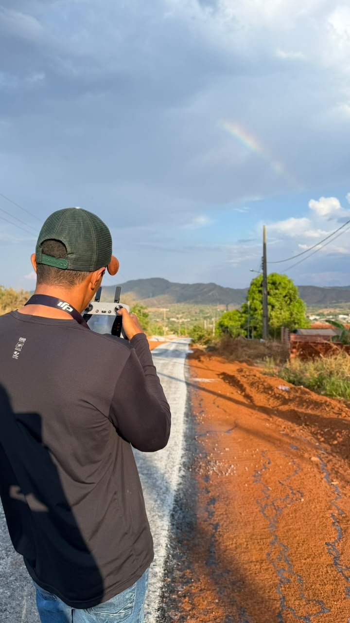 Profissional da CriaArte de costas pilotando drone numa estrada de terra, com montanhas ao fundo