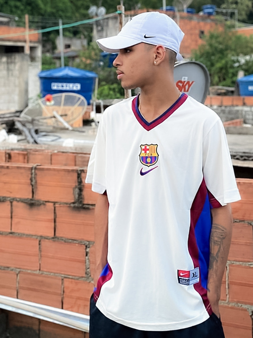 Rapaz de boné branco vestindo camisa retrô branca com detalhes grená e azul
